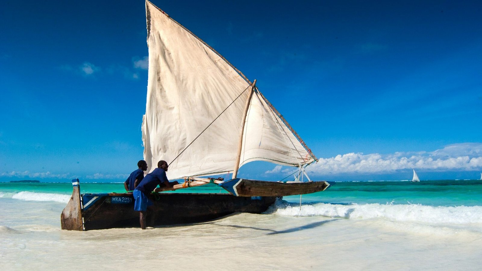 A traditional wooden dhow with its sail up on turquoise water off Zanzibar
