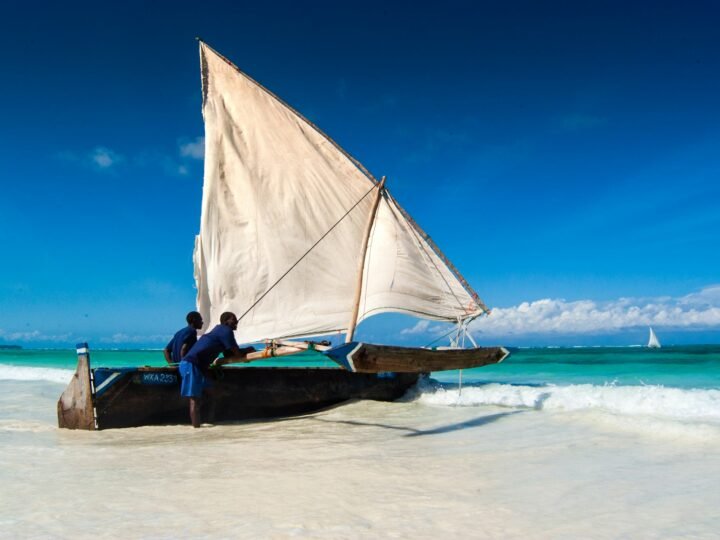 A traditional wooden dhow with its sail up on turquoise water off Zanzibar
